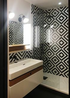 a bathroom with black and white tiles on the wall, sink and shower stall area