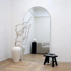 a mirror sitting on top of a wooden floor next to a white vase and table