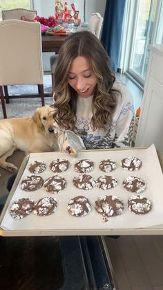 a woman holding up a tray of cookies with chocolate frosting on it and a dog sitting next to her