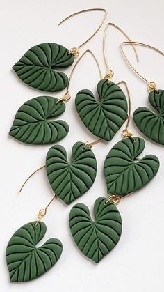 green leaf earrings are hanging from gold earwires on a white surface, with the leaves shaped like heart shapes