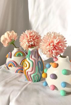 three colorful vases with flowers in them on a white surface, one has pink carnations