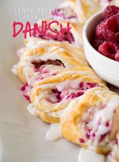 some raspberry cream cheese danish rolls on a white plate next to a bowl of raspberries