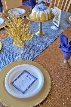 the table is set with blue and gold plates, silverware, and cake on it