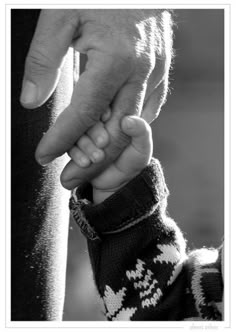 a black and white photo of a person holding the hand of a child's hand