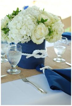 white flowers are in a blue vase on a table with silverware and napkins