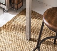 a wooden stool sitting on top of a rug next to a table with a microwave