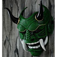 a green mask with horns on it's head is hanging from the wall in front of a black background