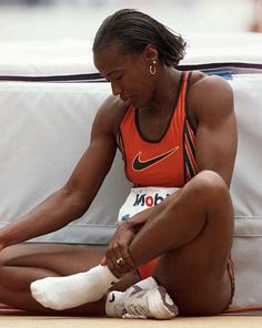 a woman is sitting on the ground with her foot in her other hand and wearing an orange top