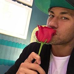 a man in a green hat is smelling a red rose