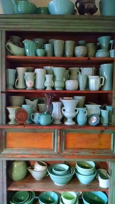 a wooden cabinet filled with lots of green dishes and cups on top of it's shelves