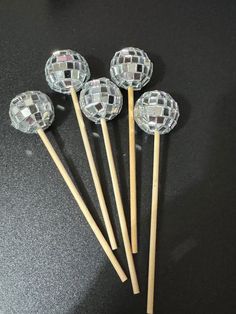 four crystal balls on wooden sticks are sitting on a black counter top, and one is in front of the other three