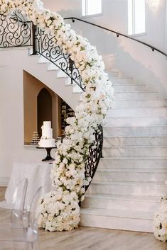 a white wedding cake sitting on top of a table next to a spiral stair case