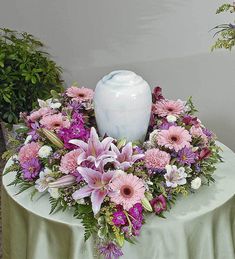 a white vase sitting on top of a table filled with flowers and greenery next to a lit candle