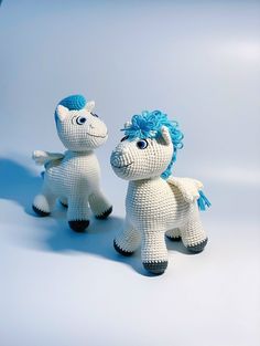 two crocheted toy horses standing next to each other on a white surface with blue hair