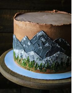 a chocolate cake with mountains on it sitting on a blue and white plate next to a wooden table