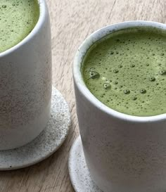 two white cups filled with green liquid on top of a wooden table