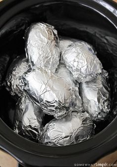 silver foil wrapped potatoes in an electric crockpot on a wooden table with text overlay