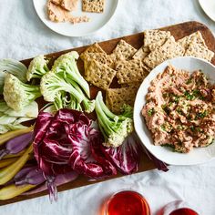 a table topped with plates of food next to wine glasses and utensils on top of a wooden cutting board