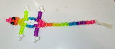 a cross made out of plastic beads on a white table with a string attached to it