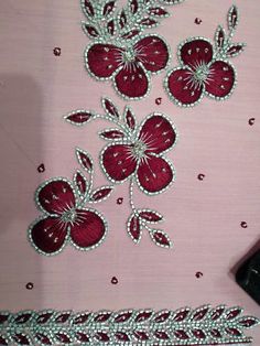 some red flowers on a pink cloth with beads and sequins next to a cell phone