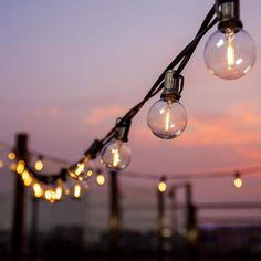 some light bulbs are hanging from a wire with lights on it at dusk or dawn