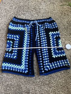 a crocheted blue and black shorts laying on the ground next to a button