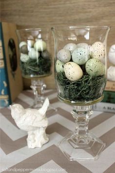 small glass vases with eggs in them on a table next to books and candles