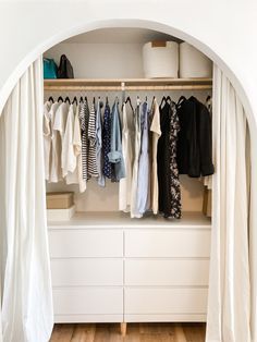 an open closet with clothes hanging on the wall and white curtains over it's doors