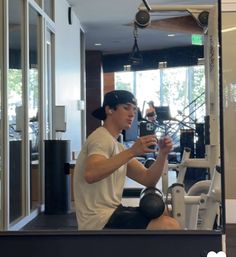 a man sitting on top of a bench in front of a gym machine holding a cell phone