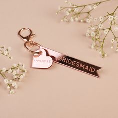 a bridesmaid keychain with a heart shaped tag on it and flowers in the background