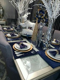 a dining room table set for christmas with silver and blue decorations