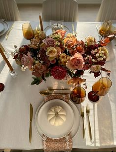 a white table topped with lots of flowers and gold place settings next to silverware