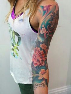 a woman wearing a white tank top with flowers on her arm and sleeve tattoo design