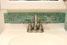 a bathroom sink with two faucets in front of a mirror and tiled back splash