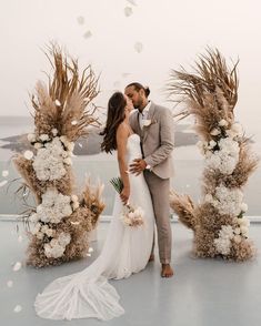 a bride and groom kissing in front of an arch of pamodia flowers with the ocean in the background