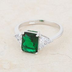 an emerald and diamond three stone ring on a marble surface with white diamonds surrounding it