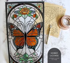 a stained glass window with an orange butterfly on it next to some crafting supplies