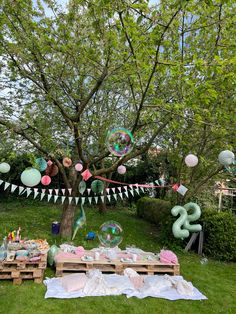 an outdoor birthday party with balloons, streamers and decorations on the grass in front of a tree