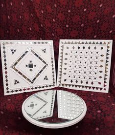 two white plates sitting next to each other on a red tablecloth covered surface with decorative designs