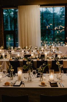 the tables are set with candles and place settings for an elegant wedding reception in front of large windows