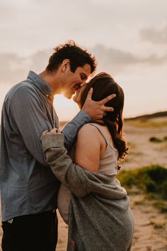 a man and woman standing next to each other in front of the ocean at sunset