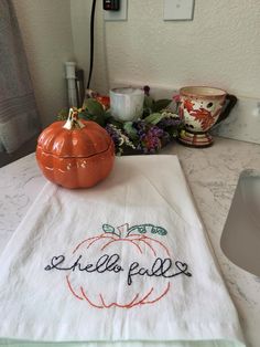 an orange pumpkin sitting on top of a kitchen counter next to a white towel with the word hello fall written on it