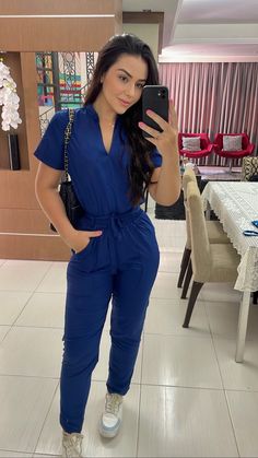 a woman taking a selfie in a blue jumpsuit with her phone up to her ear