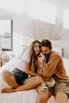 a man and woman sitting on top of a bed with a dog in their lap