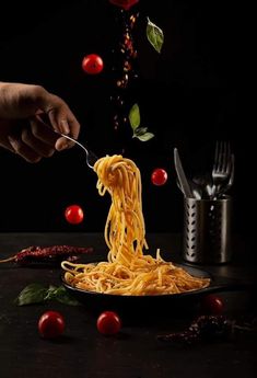 a person is eating spaghetti from a black plate with cherry tomatoes and basil on the side