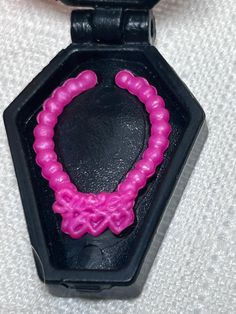 a pink beaded bracelet is attached to a black plastic case on a white surface