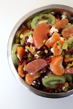 a metal bowl filled with sliced fruit and veggies on top of a white table