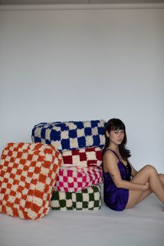 a woman is sitting on the floor next to some knitted blankets and pillows in various colors