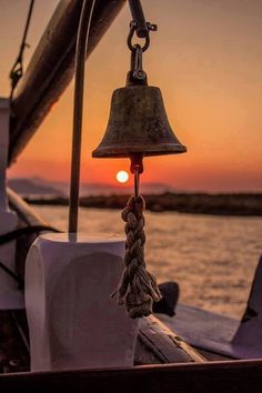 a bell hanging from the side of a boat at sunset or sunrise on the water