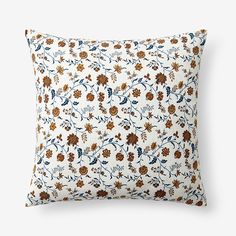 a white pillow with brown and blue flowers on the front, sitting on a white surface